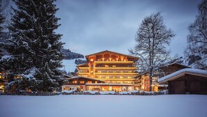 Un hotel de varios pisos con arquitectura alpina tradicional, que destaca por su entrada principal y fachada bien iluminada.