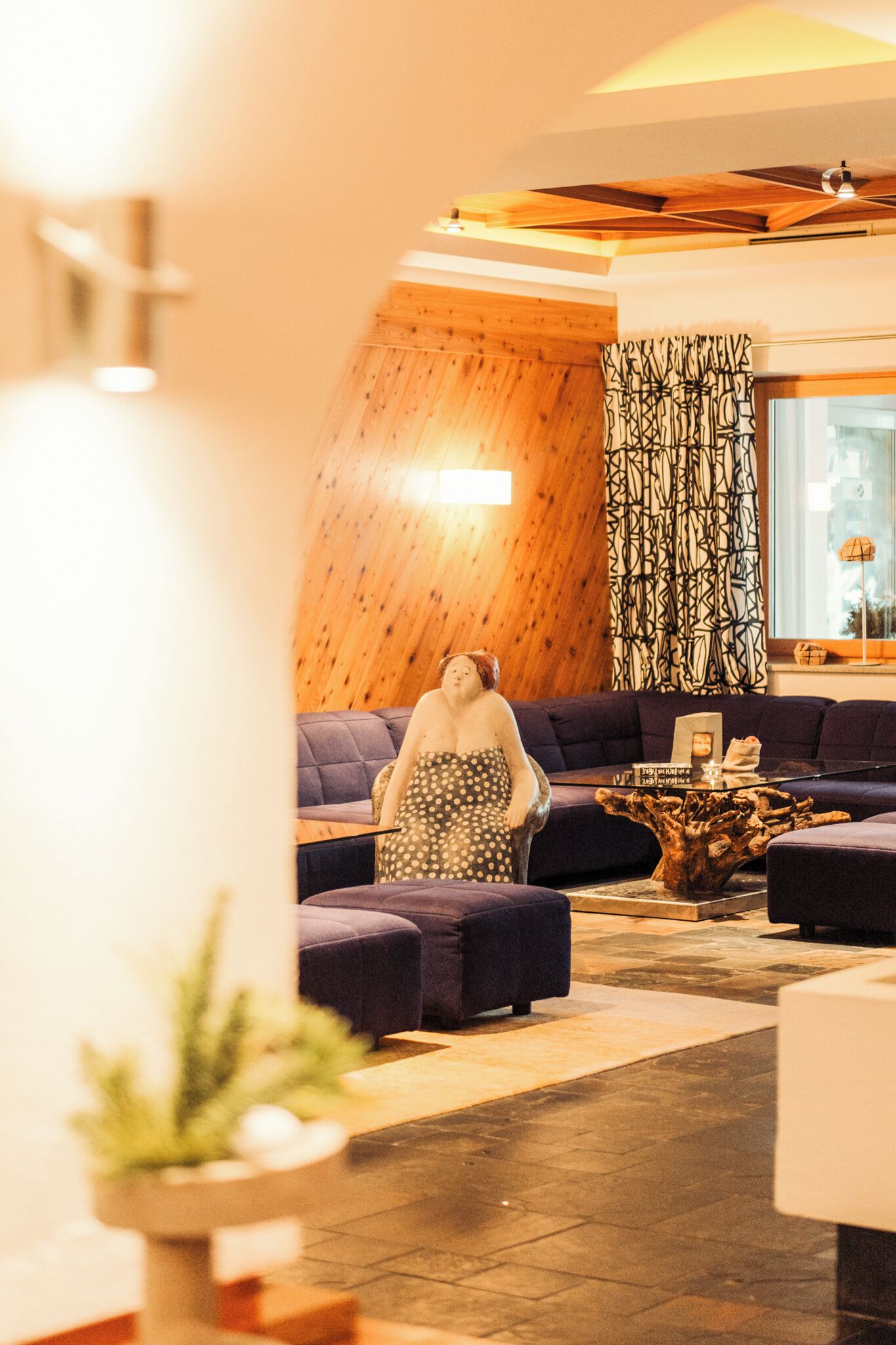 Un salon chaleureux avec un plafond en bois, un ensemble de canapés et un tronc d’arbre décoratif servant de centre de table.