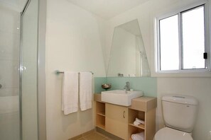 A bathroom with a glass shower enclosure, a sink with a mirror above it, and a toilet.