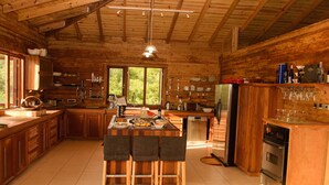 A spacious kitchen with wooden cabinets, a large island with bar stools, a refrigerator, and a dishwasher. - The Cottage, 3 Bedroom Rustic Villa (Belle Isle)