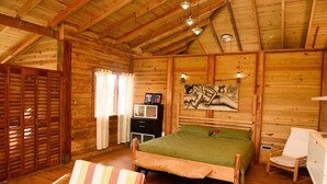 A wooden cabin bedroom with a bed, a chair, a desk, and a painting on the wall. - The Cottage, 3 Bedroom Rustic Villa (Belle Isle)