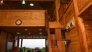 A wooden cabin interior with a large clock, a television, and a view of the outdoors. - The Cottage, 3 Bedroom Rustic Villa (Belle Isle)