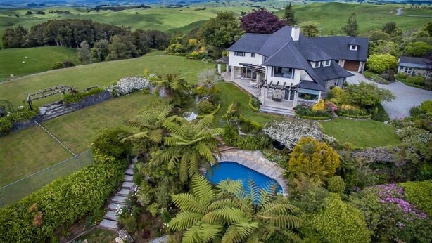 Ein großes Haus mit Schwimmbad, umgeben von üppiger Vegetation und einem malerischen Blick auf sanfte Hügel.