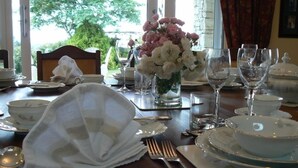 Ein Esstisch, gedeckt für eine Mahlzeit, mit Tellern, Schüsseln, Besteck und einer Blumenvase.