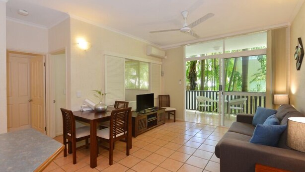 A living room with a dining area, a TV, and a balcony with a view of greenery.