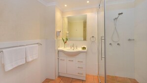 A modern bathroom with a glass shower enclosure, a white sink with a mirror above it, and a towel rack with two towels.