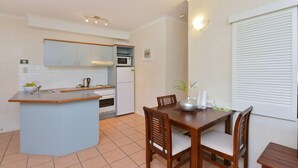 A compact kitchen with a central island, a dining table with chairs, and a window with blinds.