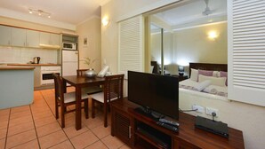 A compact hotel room with a kitchenette, a dining area, a TV, and a bed with a view.