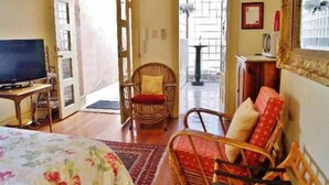 A room with a bed, a television, a wicker chair, a sofa, and a small table. - Fire Station Inn - 1 bedroom spa suite (Loggia) (Adelaide North)