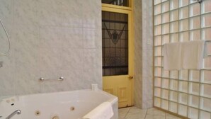 A bathroom with a large bathtub, a glass door, and a tiled wall with a towel rack. - Fire Station Inn - 1 bedroom spa suite (Loggia) (Adelaide North)