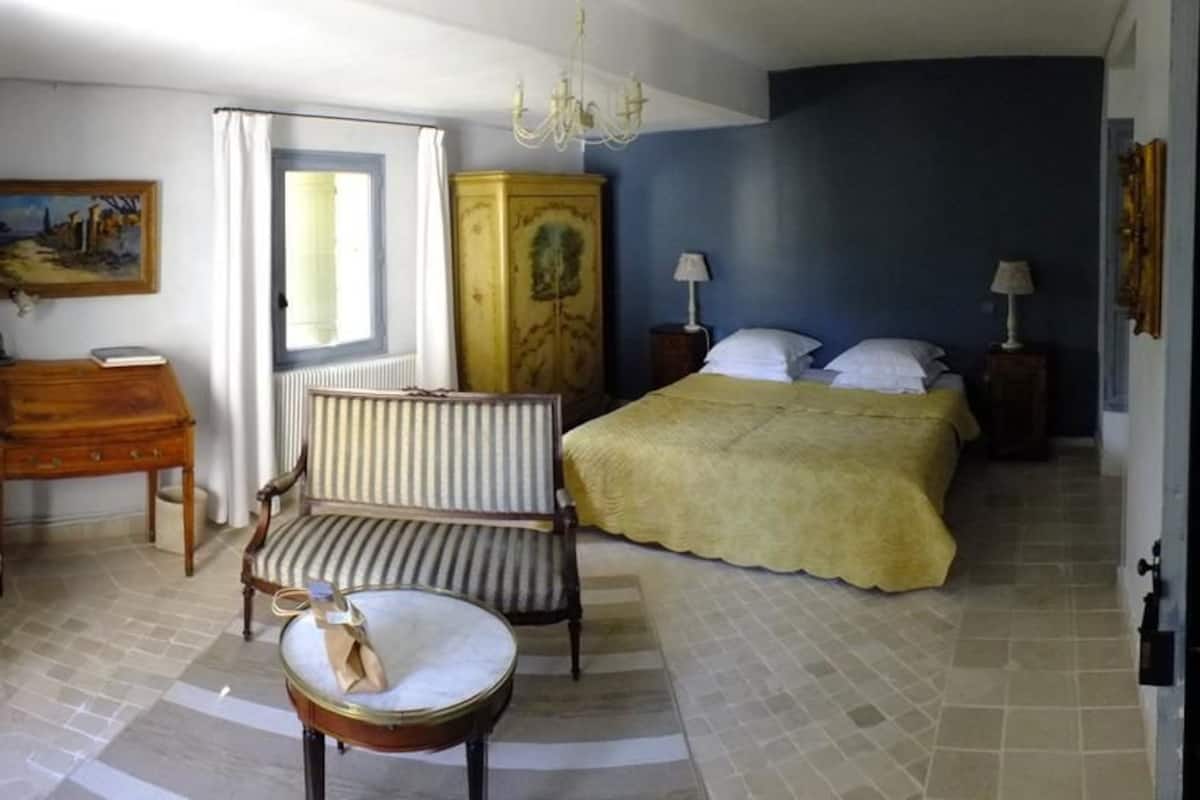 A bedroom with a bed, a chair, a small table, a cabinet, and a painting on the wall.