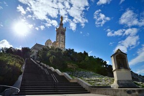 A staircase leading to a church with a bell tower and a statue on top, surrounded by greenery. - La Royante (Aubagne)