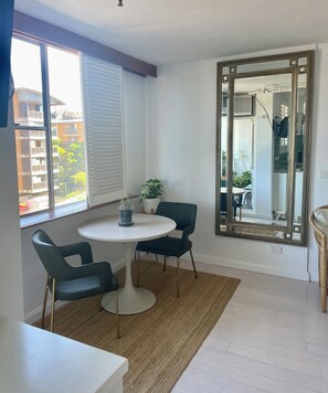 A room with a round table, two chairs, a potted plant, a large mirror, and a view of buildings outside.