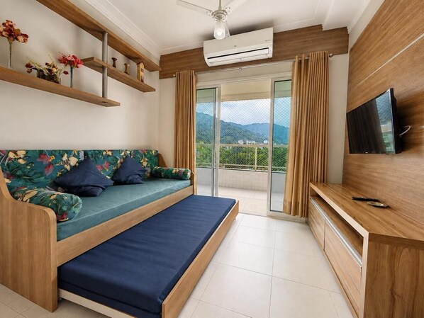 A modern bedroom with a sofa bed, a TV, and a balcony with curtains. - EXCELLENT APARTMENT 41 - SEA VIEW, TWO PARKING SPACES, ABSOLUTE HYGIENE, WE HAVE OTHER OPTIONS. (Ubatuba)