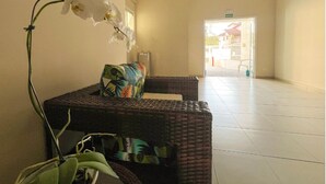 A reception area with a wicker sofa, a potted orchid, and a tiled floor. - EXCELLENT APARTMENT 41 - SEA VIEW, TWO PARKING SPACES, ABSOLUTE HYGIENE, WE HAVE OTHER OPTIONS. (Ubatuba)