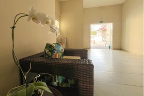 A reception area with a wicker sofa, a potted orchid, and a tiled floor. - EXCELLENT APARTMENT 41 - SEA VIEW, TWO PARKING SPACES, ABSOLUTE HYGIENE, WE HAVE OTHER OPTIONS. (Ubatuba)