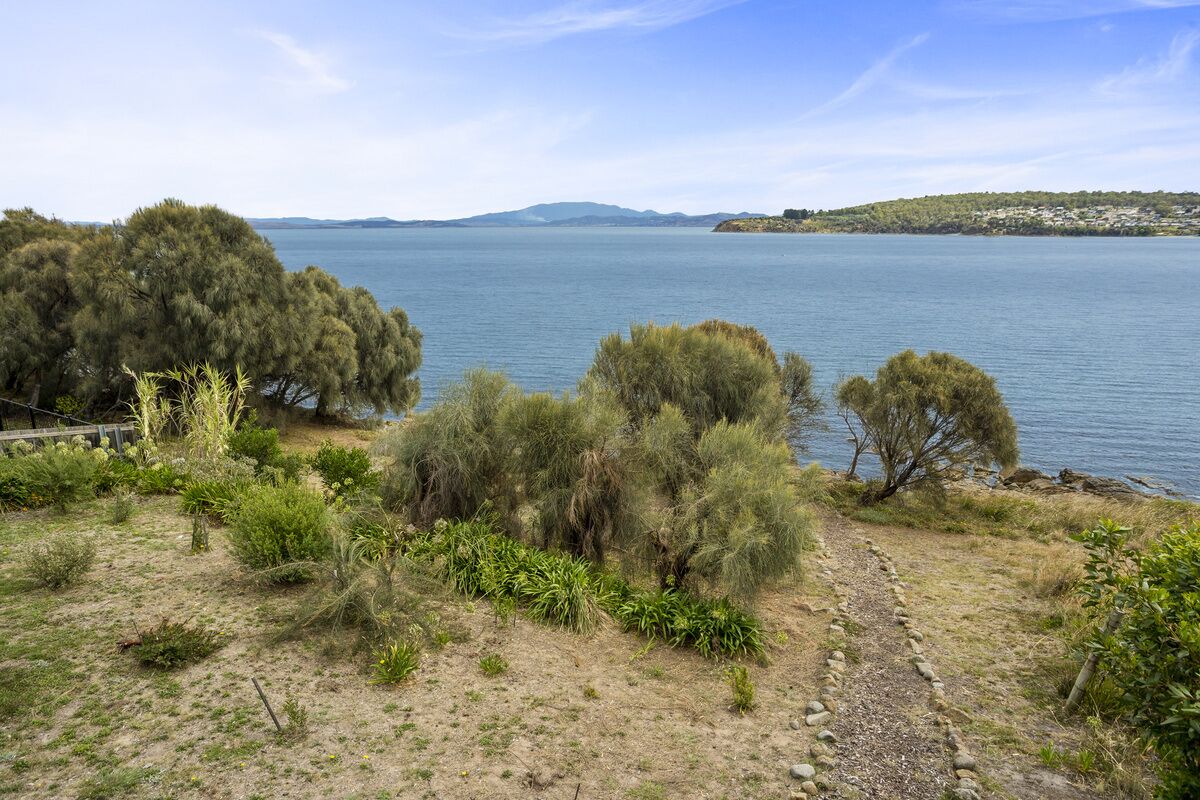 Ett kustlandskap med fri utsikt över havet, en stenig stig och tät vegetation.
