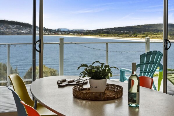 A table with a bottle, a plant, and a basket on a balcony overlooking a beach. - Dolphin View Beach House (Primrose Sands)
