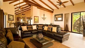 A spacious living room with a large sectional sofa, a glass coffee table, and a ceiling fan.