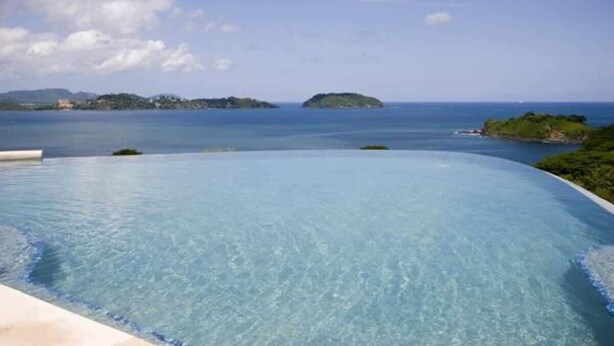 A clear blue infinity pool with a view of the sea and distant islands.