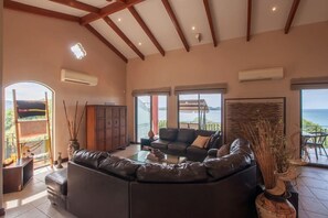 Un salón amplio con un sofá seccional grande, una mesa de centro y vistas al mar a través de grandes ventanales.