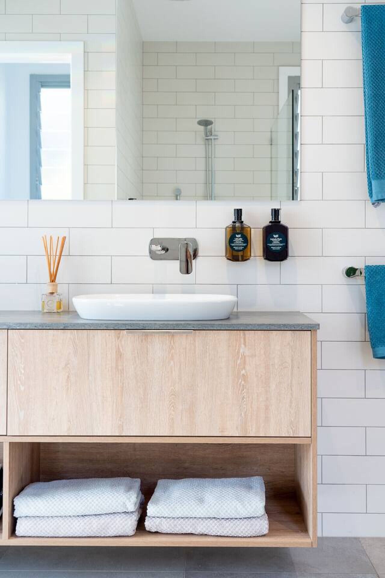 Ein modernes Badezimmer mit einem weißen Waschbecken, einer Holz-Kommode und einem Spiegel darüber. Auf der Kommode stehen zwei Seifenspender.