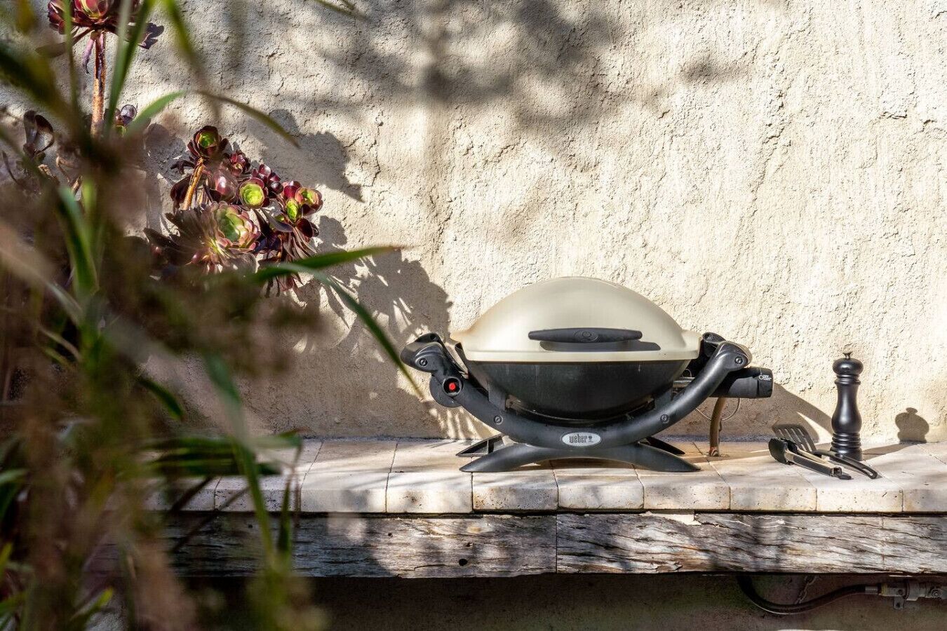 A Weber grill with a black lid, placed on a concrete surface against a textured wall.