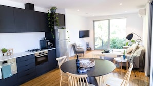 Une cuisine moderne avec des meubles de couleur sombre, un coin repas doté d’une table ronde et un espace de vie comprenant un canapé et un téléviseur.