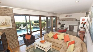 Un salon spacieux avec un grand canapé, une table basse et un téléviseur. Une porte-fenêtre coulissante donne accès à un balcon avec une piscine.