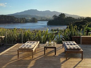 Een houten terras met twee lounge fauteuils en een tafel, met uitzicht op een rivier en verre bergen.