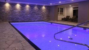 An indoor swimming pool with stone walls and a blue-lit floor. - Hotel Muschinsky (Bad Lauterberg)