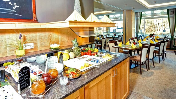 A buffet area with a variety of fruits and vegetables, a chalkboard menu, and a seating area with tables and chairs. - Hotel Muschinsky (Bad Lauterberg)