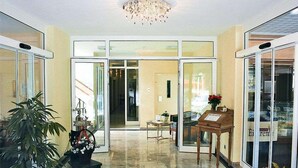 A hotel lobby with a chandelier, a reception desk, a plant, and a welcome mat. - Hotel Muschinsky (Bad Lauterberg)