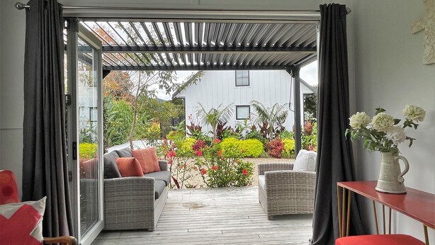 A patio area with wicker furniture, a red chair, and a table with a vase of flowers. - The Abbey - Gorgeous Living In the Village (Point Wells)