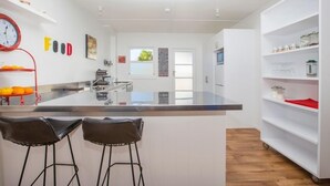 A modern kitchen with a central island, two bar stools, and a white shelving unit. - The Abbey - Gorgeous Living In the Village (Point Wells)
