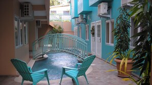 A pool area with a small bridge, two chairs, and potted plants. - Easy Walk To Store Bay, Pigeon Point, Restaurants & Entertainment (Crown Point)