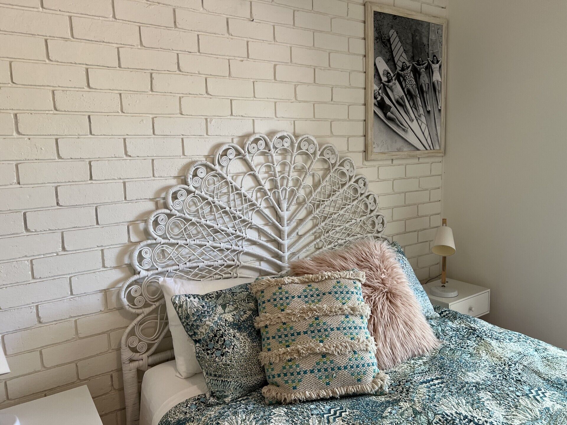 A bed with a white brick wall background, a decorative metal headboard, patterned pillows, and a framed picture on the wall.