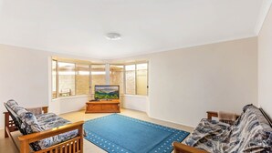 A living room with a large window, a wooden TV stand, and two sofas. - Home away from home - Close to the beach (GERRINGONG)