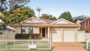 A single-story house with a tiled roof, a front garage, and a fenced yard. - Home away from home - Close to the beach (GERRINGONG)