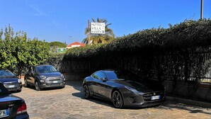 A parking area with a black sports car, a black sedan, and a blue car. There is a sign for a hotel and villa. - Hotel Villa Mary (Loano)