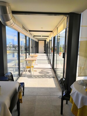 A corridor with tables and chairs, large windows, and a view of the outside. - Hotel Villa Mary (Loano)
