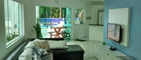 A modern living room with a sectional sofa, a flat-screen TV mounted on the wall, and a view of a pool and outdoor seating area.
