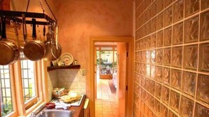 A kitchen with a long countertop, hanging pots, and a view to a dining area. - Melbourne Street Mews Spa Cottage (Adelaide City)