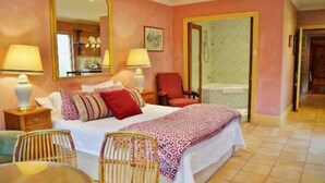 A bedroom with a bed, two bedside tables, a chair, a mirror, and a bathroom door. - Melbourne Street Mews Spa Cottage (Adelaide City)