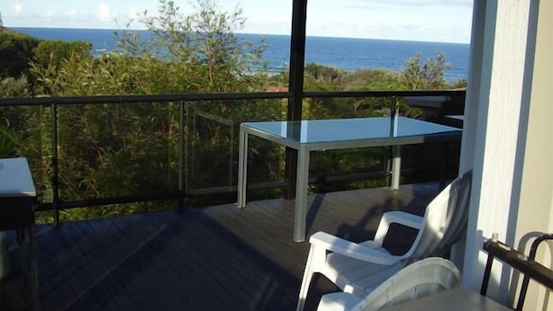 A balcony with a glass table and chairs, overlooking a coastal landscape. - STRATHMORE LODGE  UNIT 1. UPPER LEVEL. Spectacular views of Lighthouse Beach. (Port Macquarie)