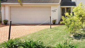 A two-story building with a white facade, a garage, and a small garden area with potted plants and a palm tree. - STRATHMORE LODGE  UNIT 1. UPPER LEVEL. Spectacular views of Lighthouse Beach. (Port Macquarie)