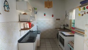 A compact kitchen with white cabinets, a microwave, a stove, and a refrigerator. There are small potted plants on the wall and a hanging light fixture. - House in Boracéia II with Pool, 3 Bedrooms (2 Suites), Billiard Table, 4 Bathrooms (São Sebastião)