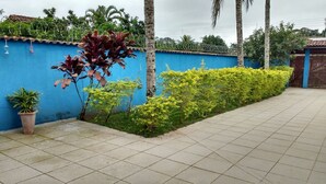 A tiled patio area with a blue wall, a metal gate, and various plants. - House in Boracéia II with Pool, 3 Bedrooms (2 Suites), Billiard Table, 4 Bathrooms (São Sebastião)