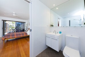 Quarto moderno com cama, banheiro com pia e vaso sanitário, e porta de vidro que dá para uma área externa.