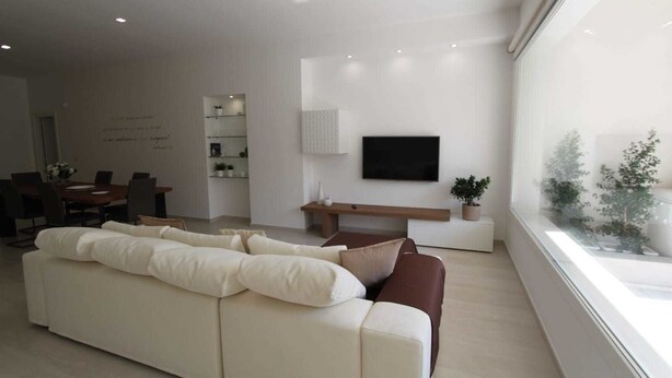 A modern living room with a large white sofa, a small coffee table, and a flat-screen TV mounted on the wall. - Bed and breakfast Ledwars (Taviano)
